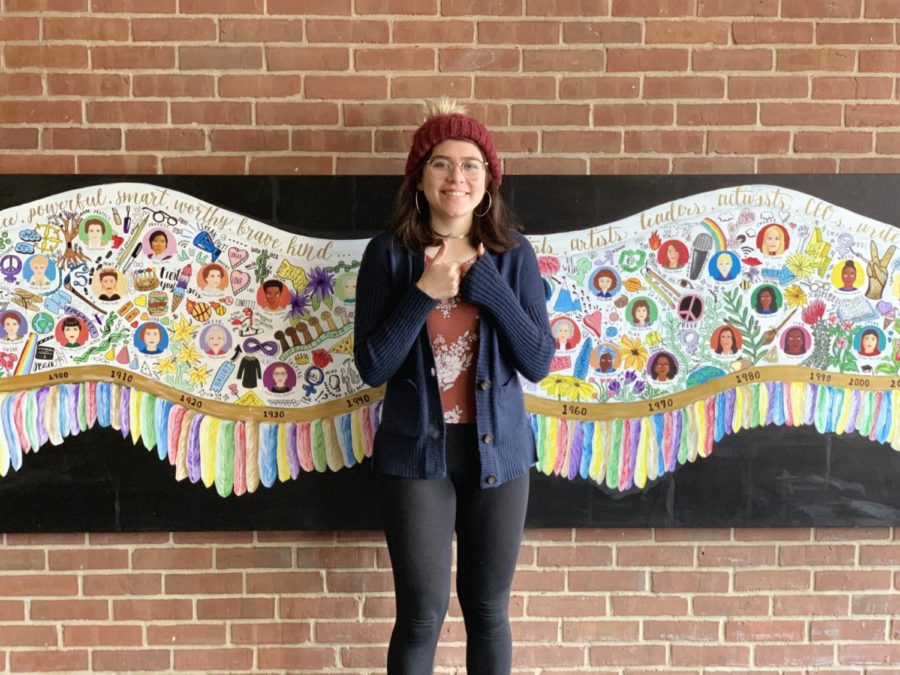 Spreading my wings-- Junior Sophie Shack smiles for a picture in front of a mural she designed for her Government and Law class. The project features 30 famous women and can be found in the alcove near the library and cafeteria. Viewers can center themselves between the wings and become a part of the narrative.